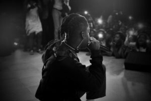 Side view of black and white unrecognizable African American singer with dreadlocks performing song on stage with microphone in hand during concert