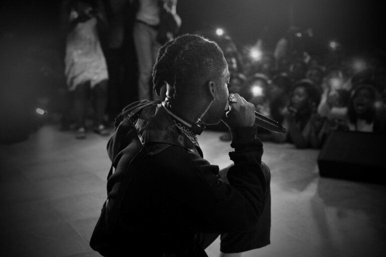 Side view of black and white unrecognizable African American singer with dreadlocks performing song on stage with microphone in hand during concert